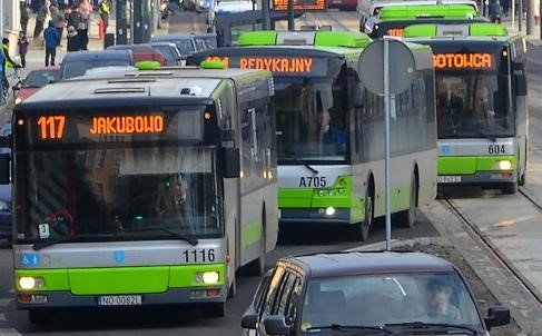 Zielono-srebrne autobusy miejskie w Olsztynie jadące w kolumnie przez miasto.