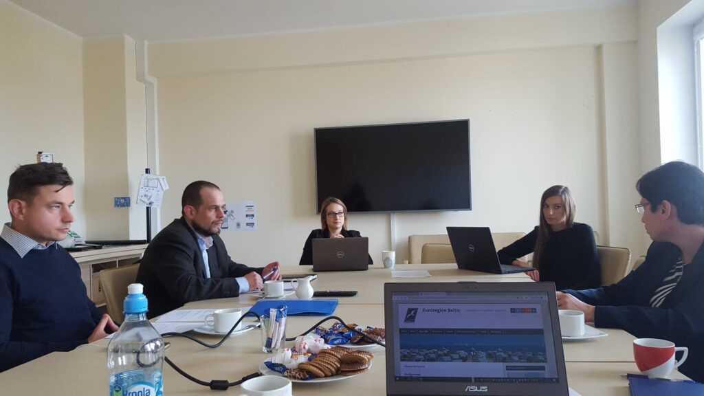 Spotkanie zespołu przy stole konferencyjnym z widocznym na laptopie portalem Euroregion Baltic.